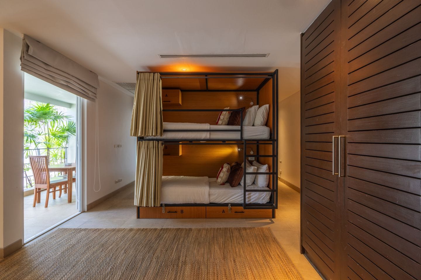 Modern dorm room with made-up bunk beds, privacy curtains and a balcony overlooking the garden